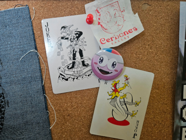 a corkboard with two joker cards, a pin of marx from the kirby series, and a clipping of a jester from a paper bag